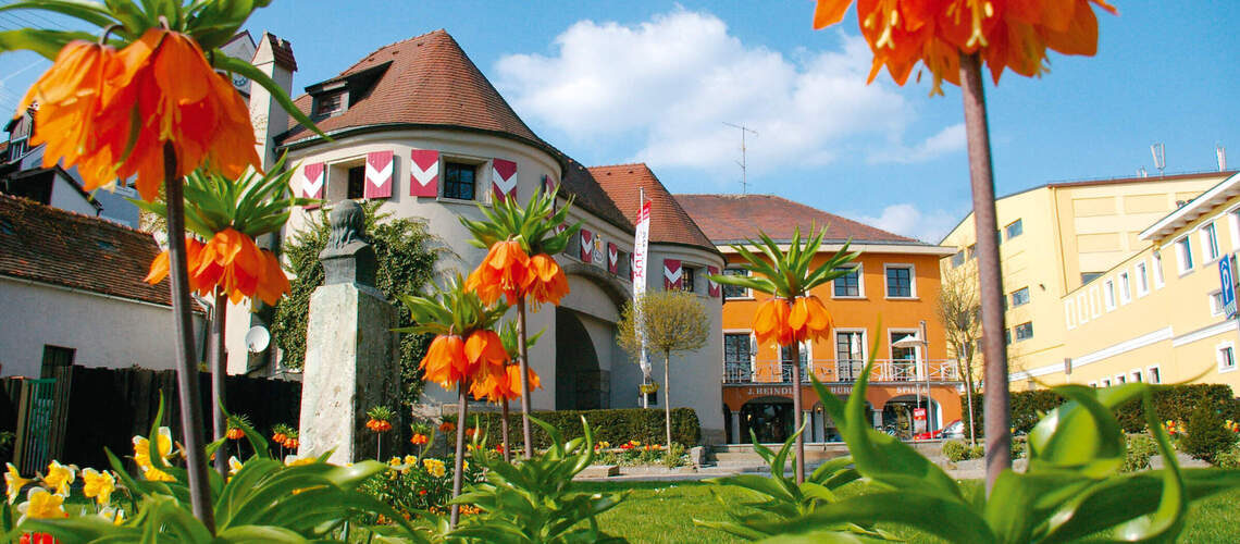 Das Linzer Tor in Schärding im Tageslicht mit strahlend blauem Himmel und blühenden orangen Blumen.