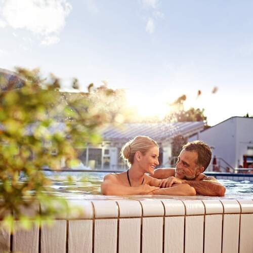 Ein Paar mit strahlenden Gesichtern genießt das sprudelnde Thermalbad in der Therme Eins Bad Füssing.